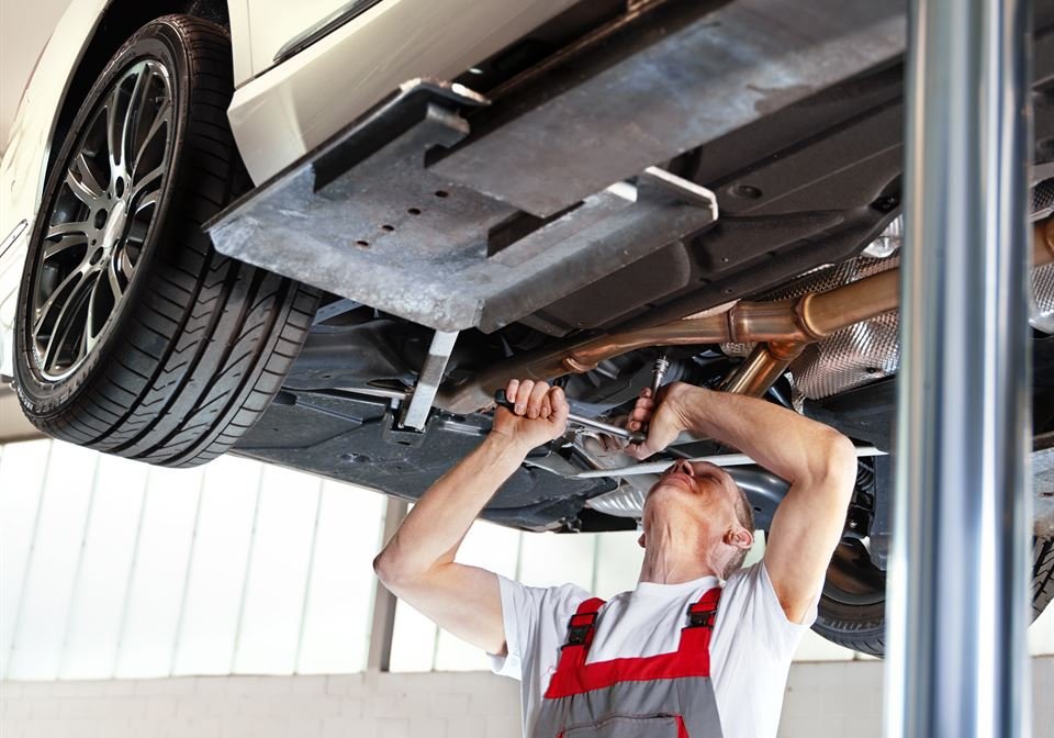 Mechaniker arbeitet unter einem Auto auf der Hebebühne